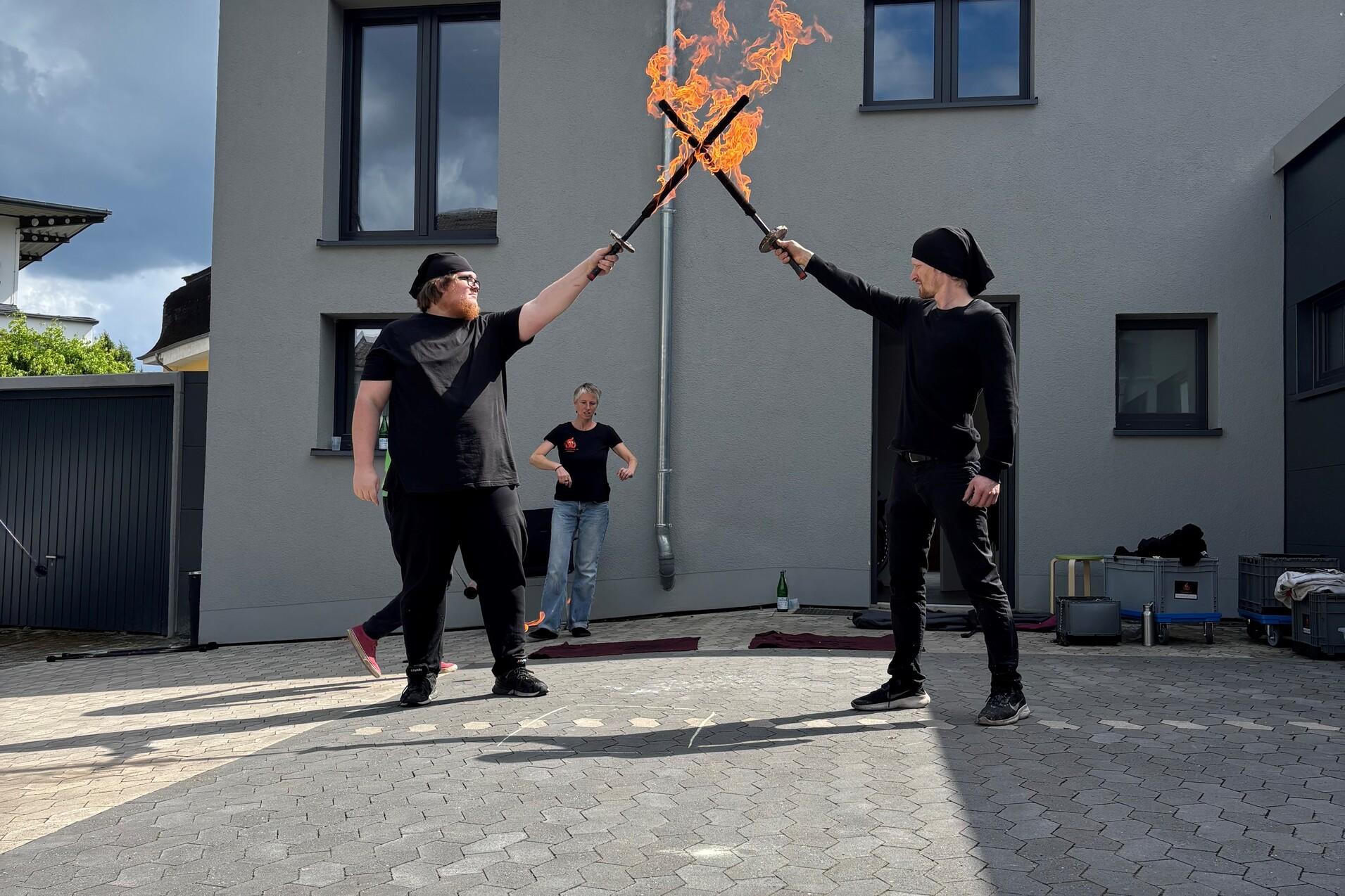 Auf dem Bild sieht man zwei junge Männer mit brennenden Feuerschwertern