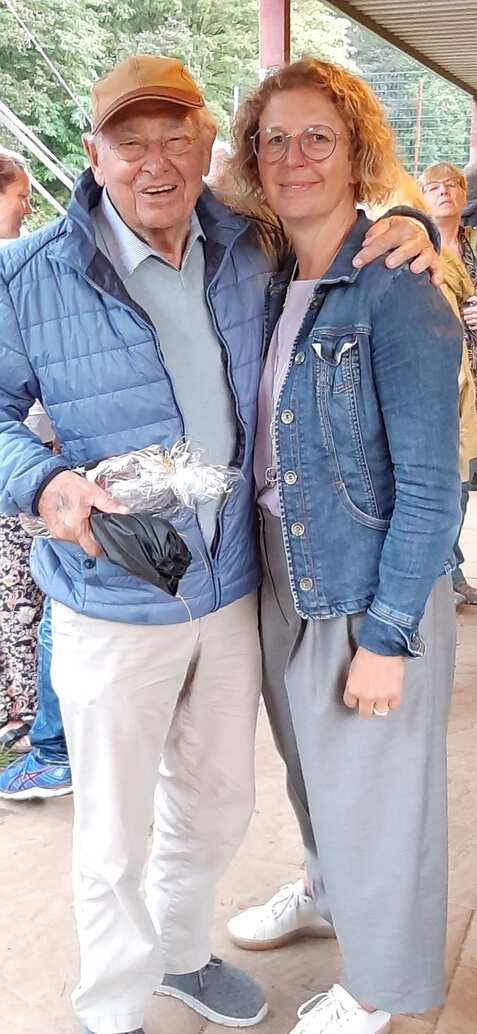 Lächelndes älteres Paar umarmt sich, der Mann trägt eine Mütze und eine Jacke, die Frau trägt eine Jeansjacke.