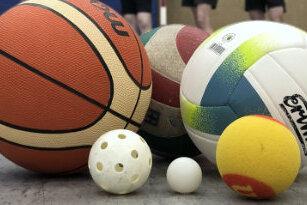 Vielf&auml;ltige Sportb&auml;lle, darunter Basketball, Volleyball und Tischtennisball, liegen auf dem Boden einer Sporthalle.