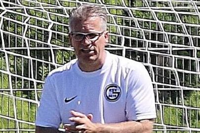 Mann in Trainingsbekleidung steht neben einem Fu&szlig;balltor und clapt begeistert, im Hintergrund ein Fu&szlig;ballfeld.