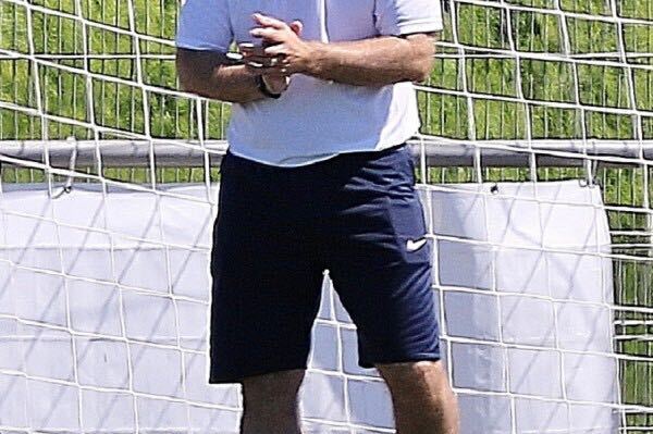 Mann in Trainingsbekleidung steht neben einem Fußballtor und clapt begeistert, im Hintergrund ein Fußballfeld.