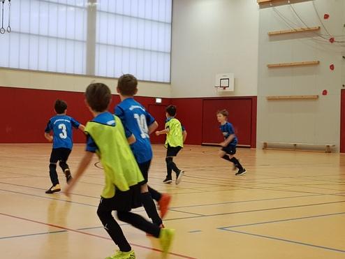 Gruppe von Jungen in blauen Trikots spielt in einer Sporthalle, einige tragen gelbe Überziehjerse.