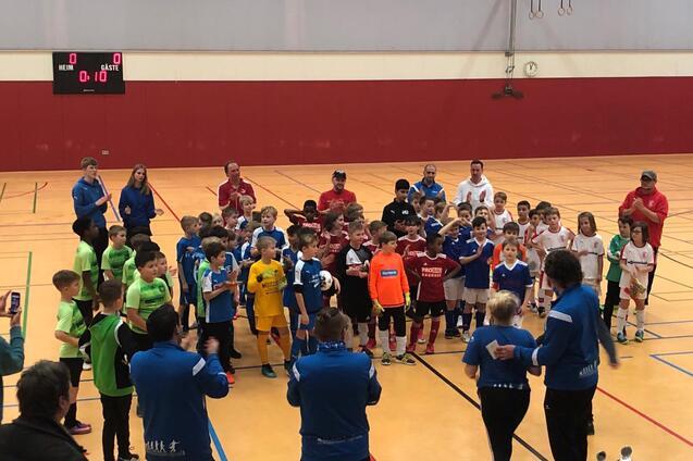 Gruppierung von Kindern in Fußballtrikots nach einem Turnier, applaudiert von Trainern in einer Sporthalle.