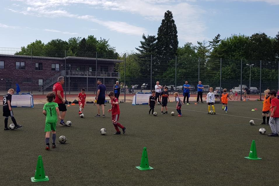 Gruppentraining von Kindern auf einem Fußballplatz, mit Coaches und Toren im Hintergrund.