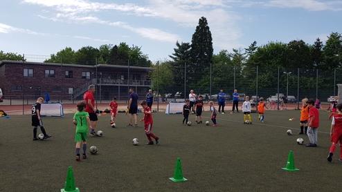 Gruppentraining von Kindern auf einem Fußballplatz, mit Coaches und Toren im Hintergrund.