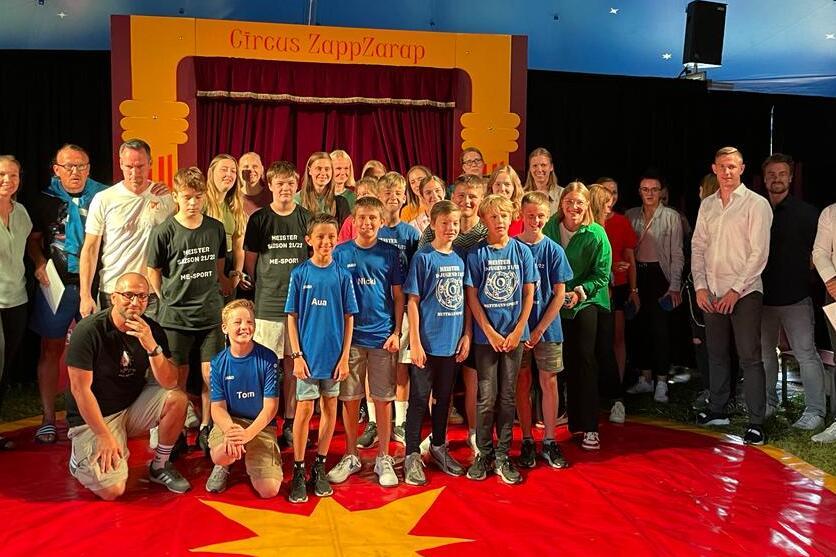 Gruppensfoto von Kindern und Erwachsenen im Zirkuszelt vor einer Bühne mit dem Schriftzug „Circus ZappZarap“.