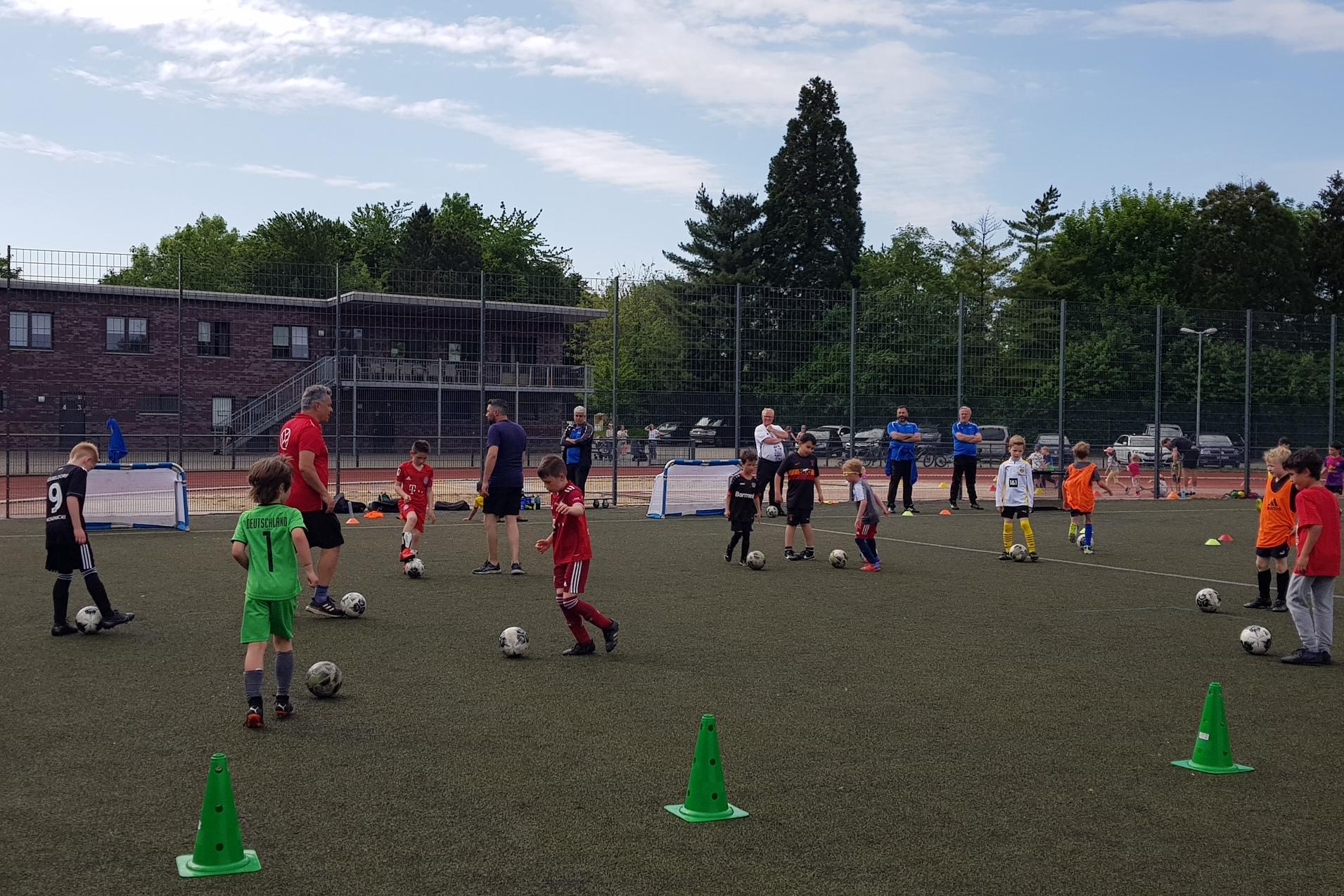 Gruppentraining von Kindern auf einem Fußballplatz, mit Coaches und Toren im Hintergrund.