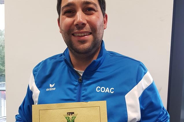 Mann in blauer Sportjacke h&auml;lt stolz ein Zertifikat f&uuml;r Kindertraining in der Fu&szlig;balleinrichtung.