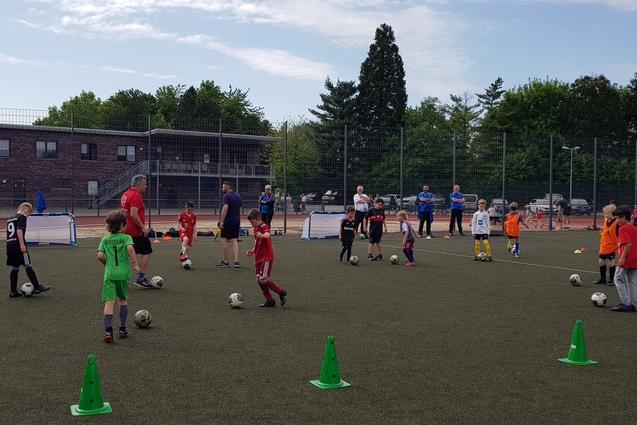 Gruppentraining von Kindern auf einem Fu&szlig;ballplatz, mit Coaches und Toren im Hintergrund.