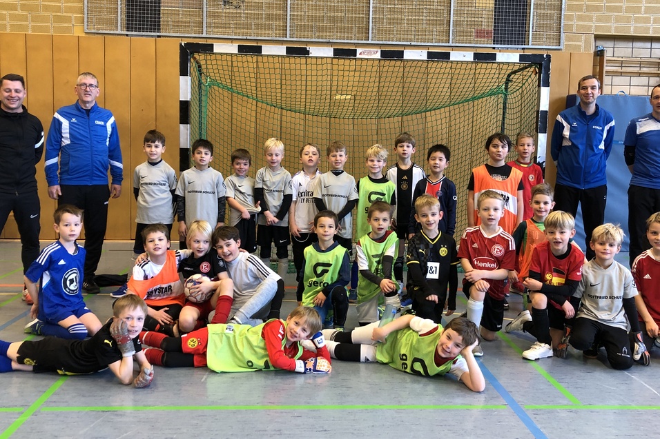 Gruppenfoto von Kindern in Fußballtrikots und Trainern vor einem Tor in einer Sporthalle.