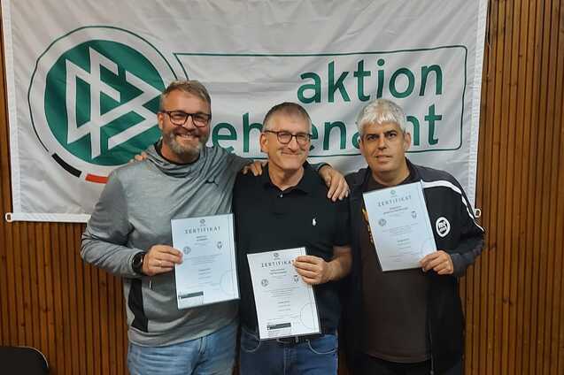 Drei Männer halten Urkunden in den Händen, stehend vor einem Banner mit der Aufschrift „aktion ehrenamt“.