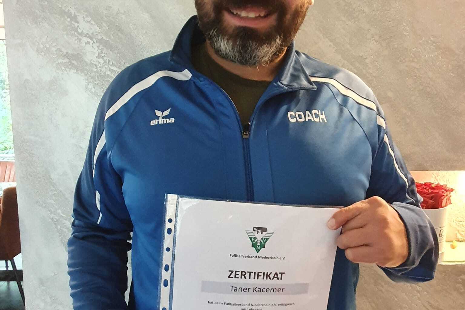 Mann in blauer Trainerjacke hält ein Zertifikat für die Ausbildung zum Kindertrainer in der Hand.