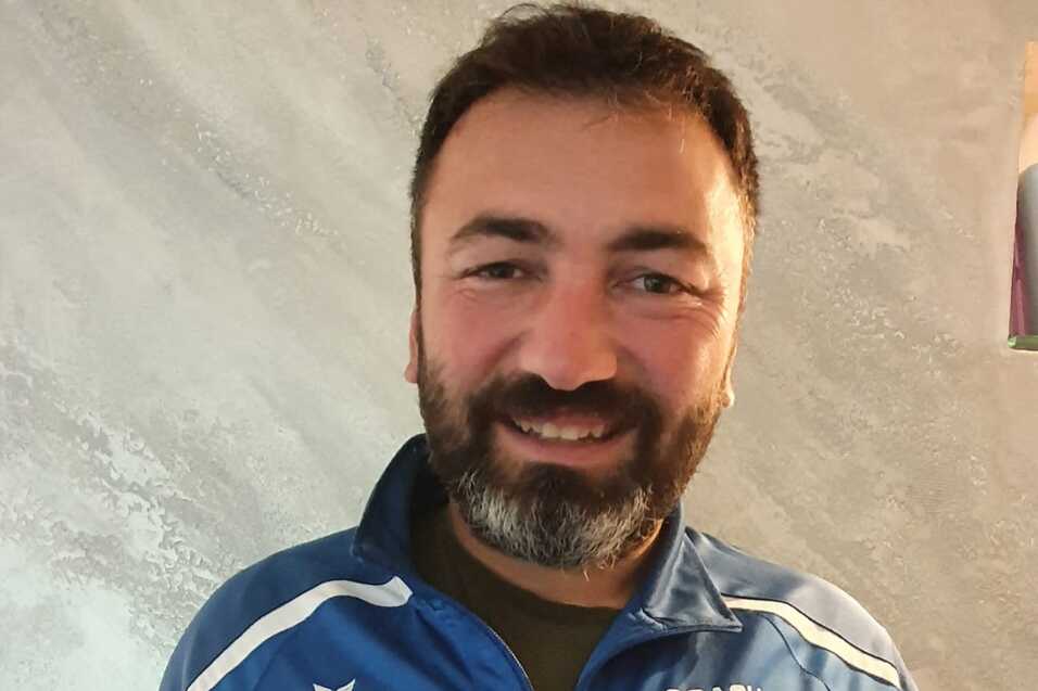 Mann in blauer Trainerjacke hält ein Zertifikat für die Ausbildung zum Kindertrainer in der Hand.