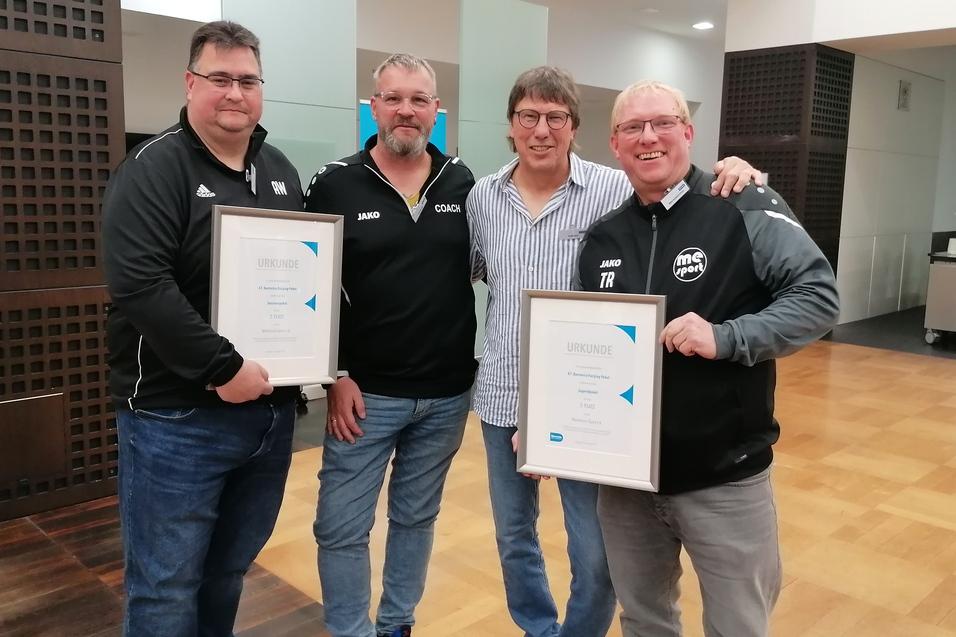 Vier Männer stehen in einem Innenraum und halten Urkunden in den Händen, lächelnd und in sportlicher Kleidung.