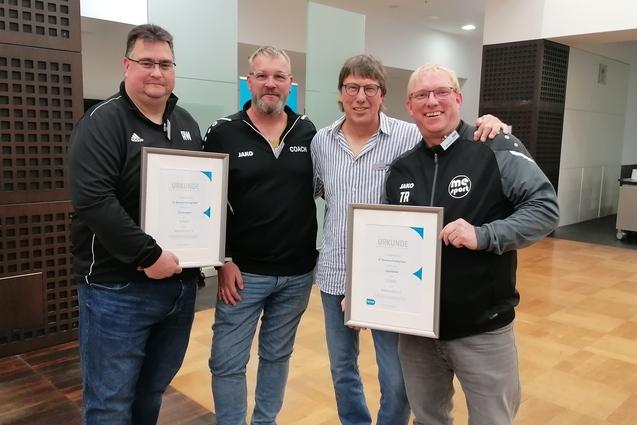 Vier M&auml;nner stehen in einem Innenraum und halten Urkunden in den H&auml;nden, l&auml;chelnd und in sportlicher Kleidung.