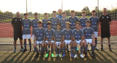 Mannschaftsfoto einer Jugend-Fußballmannschaft mit Trainer vor einem Tor auf einem Sportplatz.