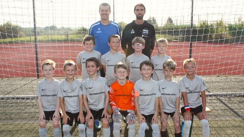 Kinderfußballmannschaft in grauen Trikots posiert vor einem Fußballtor auf einem Kunstrasenplatz.
