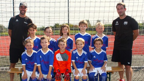 Gruppenshot einer Jugendfußballmannschaft in blauen Trikots, zwei Trainer stehen hinter den Spielern vor einem Tor.