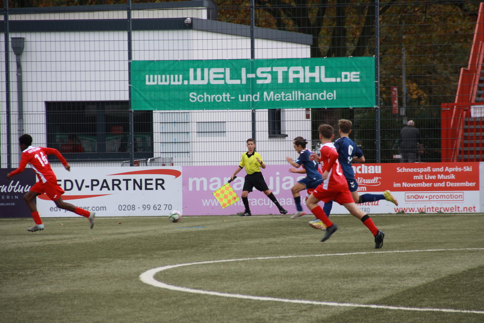 Junger Fußballspieler in roter Uniform sprintet während eines Spiels über den Kunstrasen, Schiedsrichter beobachtet.