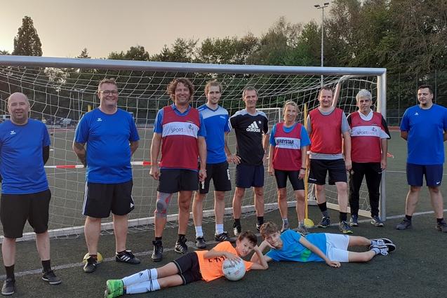Gruppenshooting von Fu&szlig;ballspielenden Erwachsenen und Kindern vor einem Tor auf einem Kunstrasenplatz.