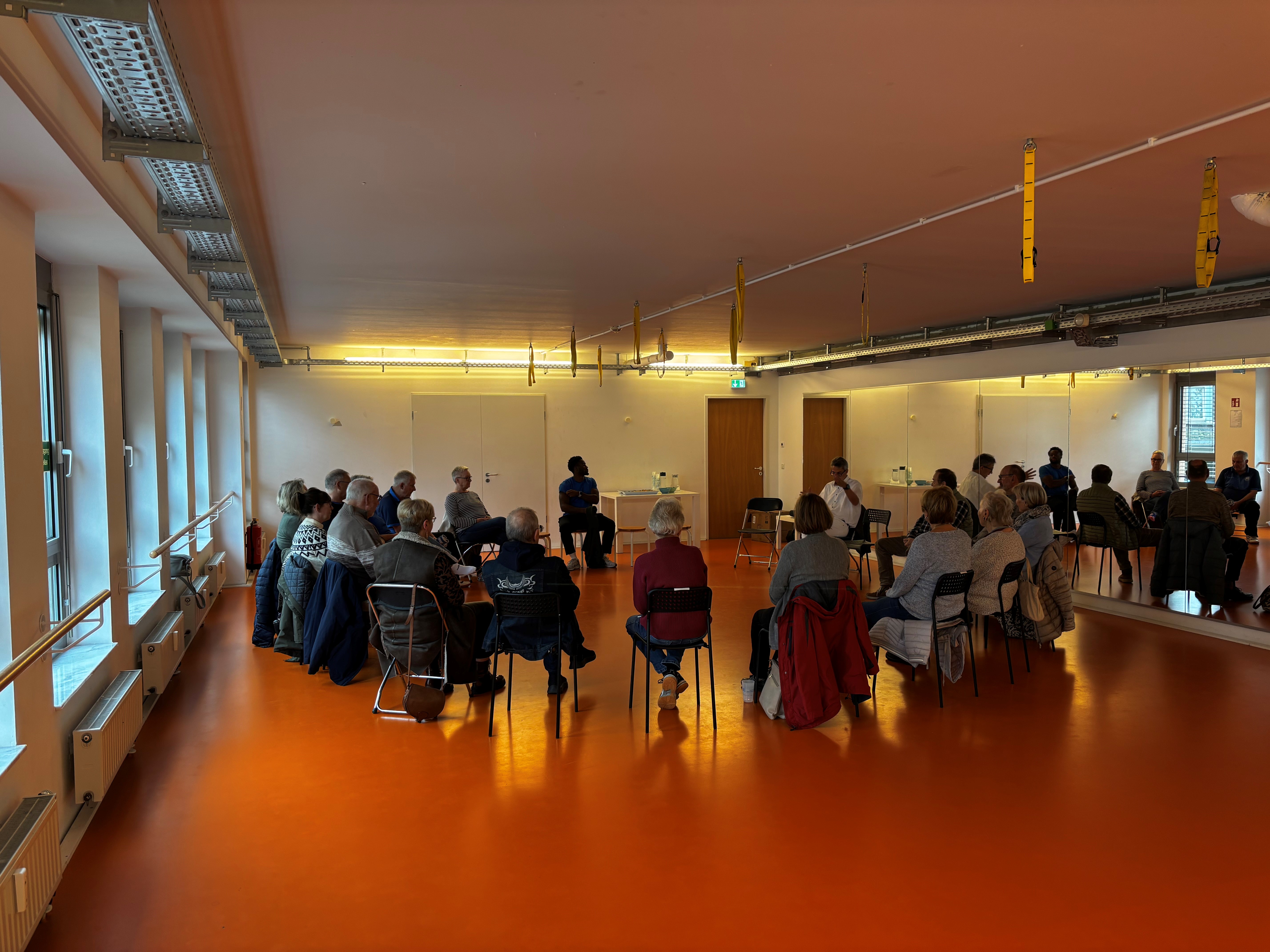 Menschen folgen sitzend im Kreis den Worten von Hr. Kober