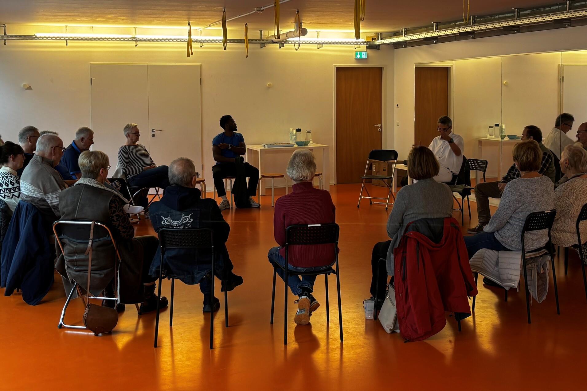 Menschen folgen sitzend im Kreis den Worten von Hr. Kober