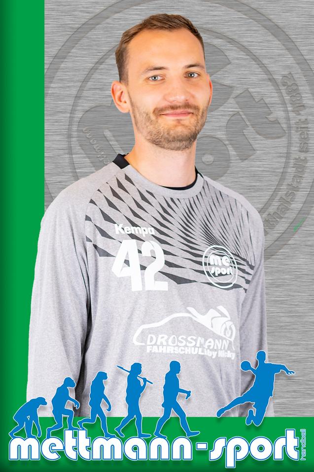 Nahaufnahme eines lächelnden Mannes in grauem Trikot mit der Nummer 42, Hintergrund in den Farben grün und silber.