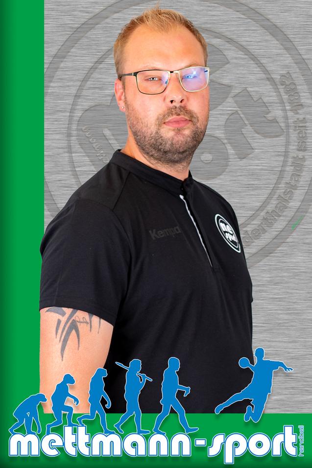 Porträt eines Mannes in schwarzem Shirt mit Brille, seitlich vor einem grauen Hintergrund mit grünem Rand.