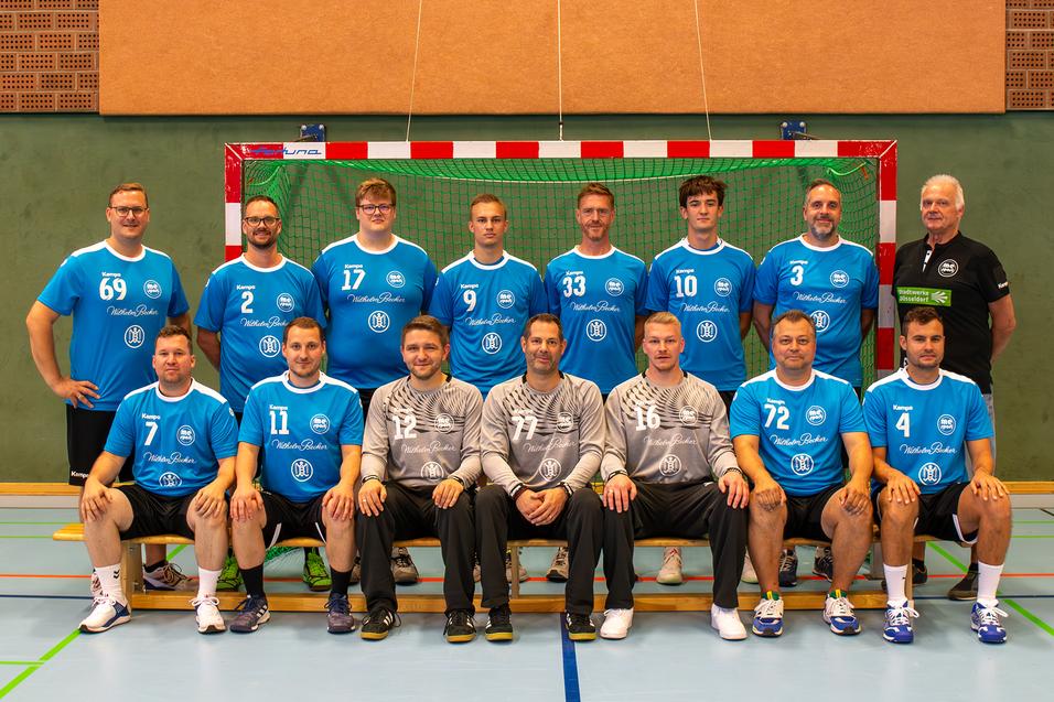 Mannschaftsfoto einer Handballmannschaft in blauen Trikots vor einem Tor in der Sporthalle.