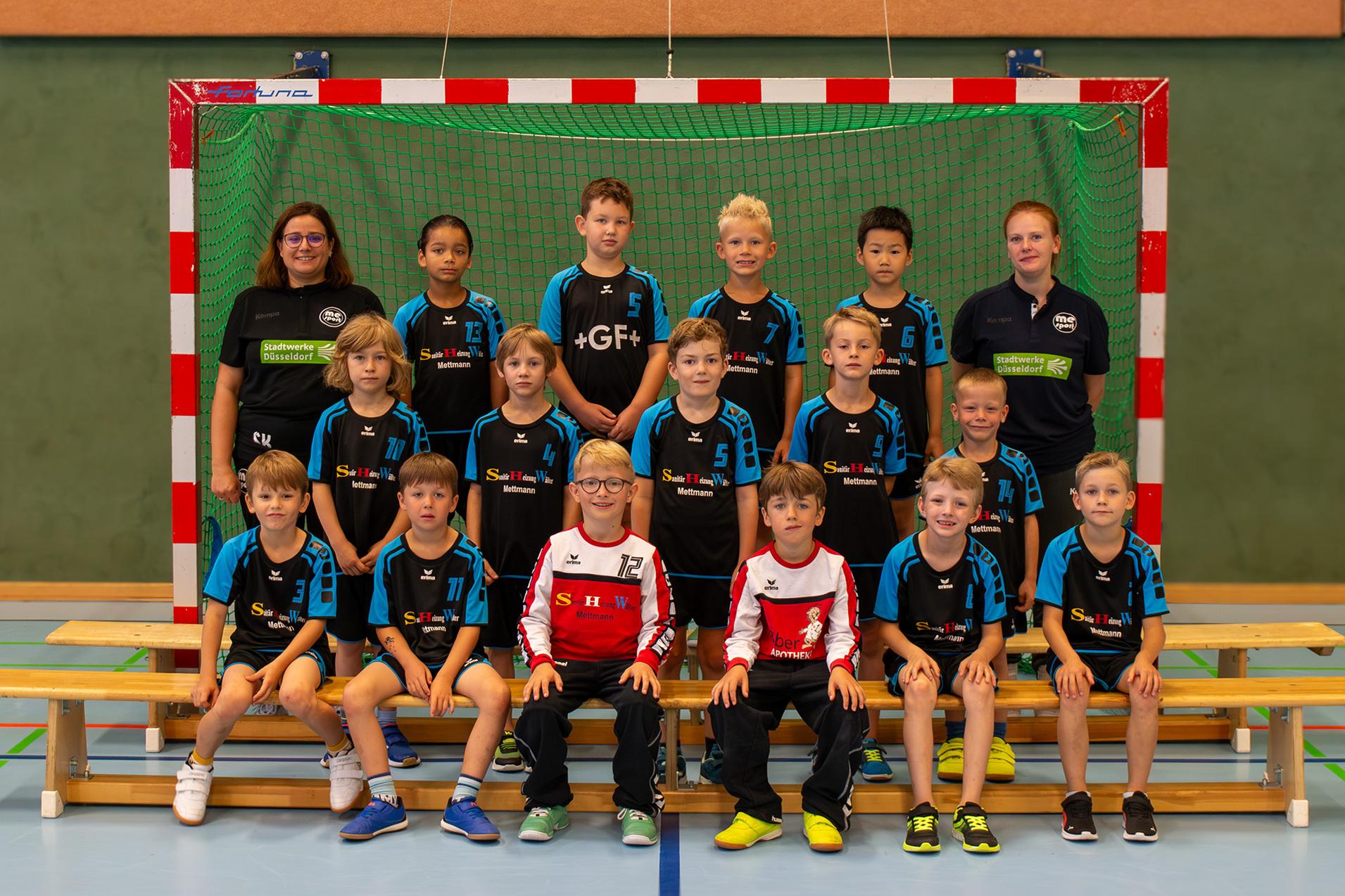 Gruppenfoto einer Jugend-Handballmannschaft mit zwei Trainerinnen vor einem Tor in einer Sporthalle.