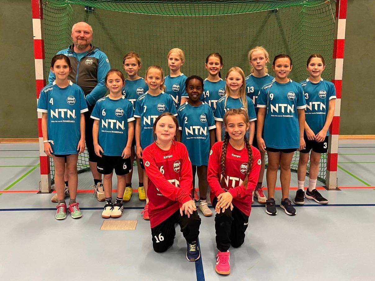 Mannschaftsfoto einer Handball-Jugendgruppe mit Trainer, alle tragen Teambekleidung in Blau und Rot.