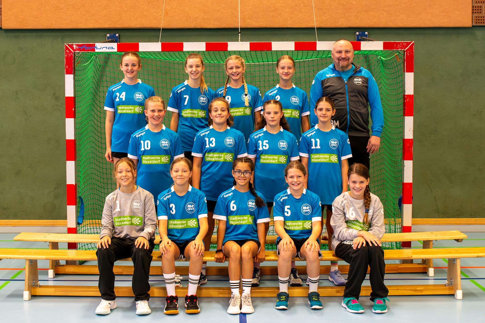 Mannschaftsfoto einer Handball-Teamgruppe mit Mädchen in blauen Trikots vor einem Handballtor.