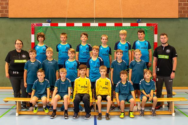 Mannschaftsfoto einer Handball-Jugend, bestehend aus 15 Jungen und 2 Betreuern vor einem Handballtor in einer Sporthalle.