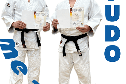 Zwei Judoka in weißen Anzügen halten Urkunden in der Hand und stehen nebeneinander. Text auf dem Bild: "JUDO".