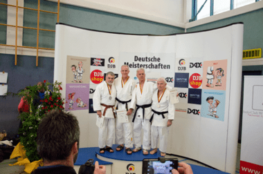 Vier Judokas in weißen Anzügen und Medaillen stehen vor einer Sponsorentafel bei den Deutschen Meisterschaften.