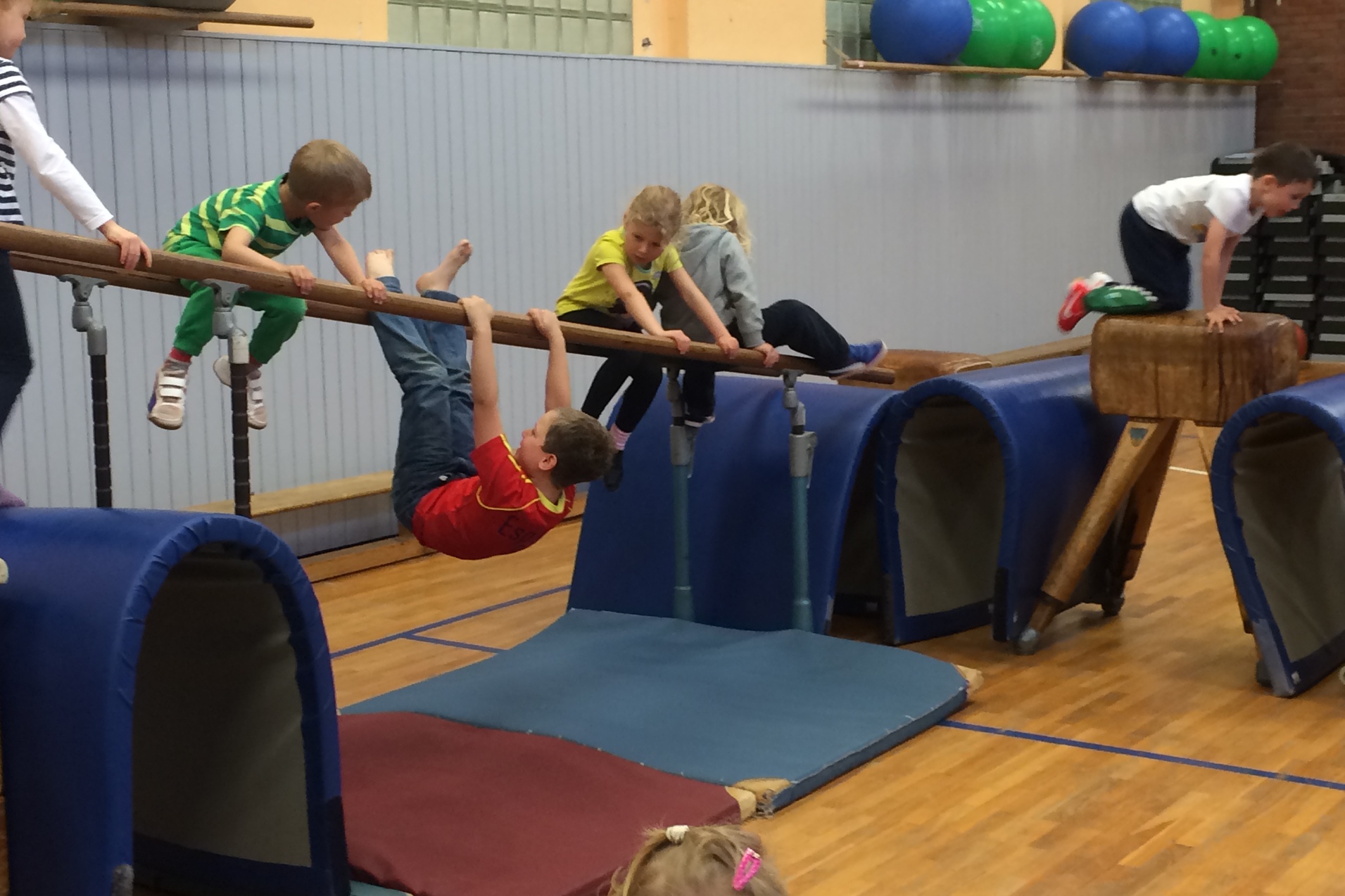 Sechs Kinder spielen in einer Turnhalle, klettern und hangeln an einem Geräteständer.