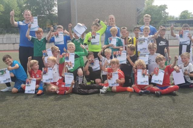 Gruppennahaufnahme von Kindern und Trainern auf einem Fußballplatz, alle halten stolz ihre Urkunden in die Höhe.