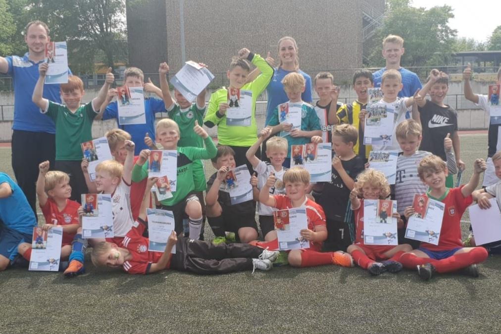 Gruppennahaufnahme von Kindern und Trainern auf einem Fu&szlig;ballplatz, alle halten stolz ihre Urkunden in die H&ouml;he.
