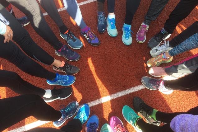 Kreis aus verschiedenen Sportschuhen auf einer roten Laufbahn, umgeben von Sportlerbeinen in Leggings.