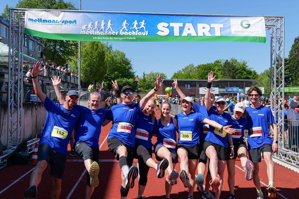 Gruppenselfie von Läufern in blauen T-Shirts, die fröhlich vor dem Startbanner eines Wettlaufs posieren.