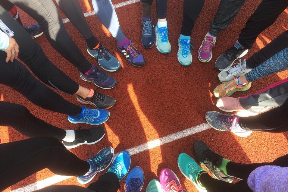 Kreis aus verschiedenen Sportschuhen auf einer roten Laufbahn, umgeben von Sportlerbeinen in Leggings.
