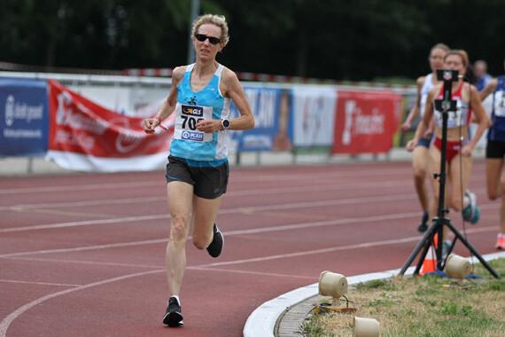 Eine Athletin in blauer Sportbekleidung sprintet auf einer Laufbahn, während andere Teilnehmer im Hintergrund laufen.