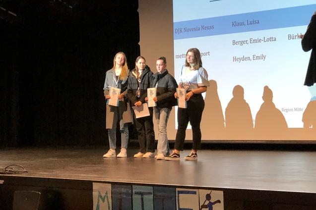 Vier junge Frauen stehen auf einer Bühne und halten Urkunden während einer Preisverleihung.