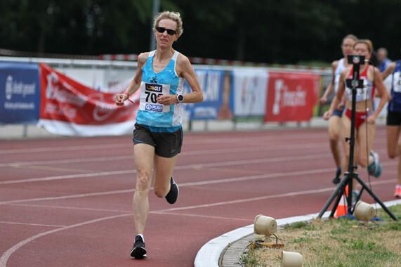 Eine Athletin in blauer Sportbekleidung sprintet auf einer Laufbahn, während andere Teilnehmer im Hintergrund laufen.