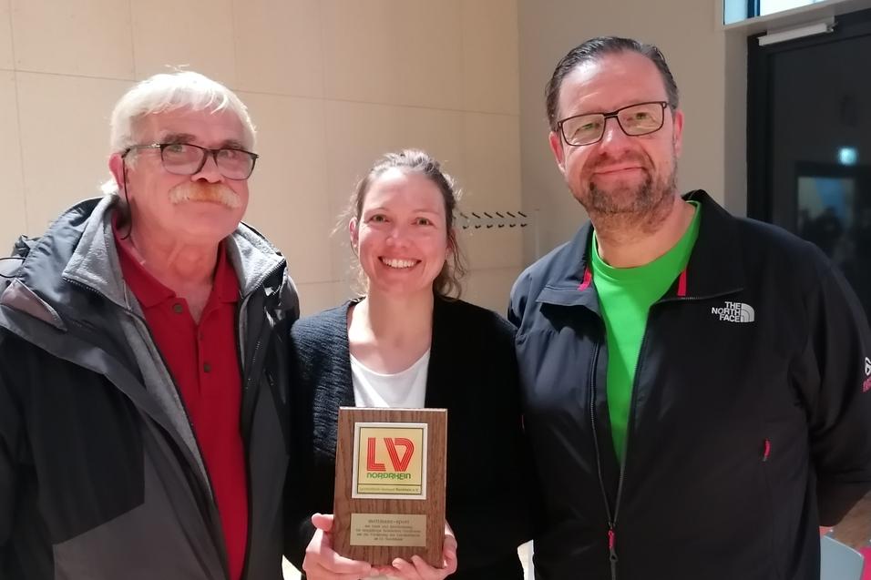Drei Personen stehen lächelnd zusammen und halten eine Auszeichnung mit dem Logo „LV Nordrhein“.