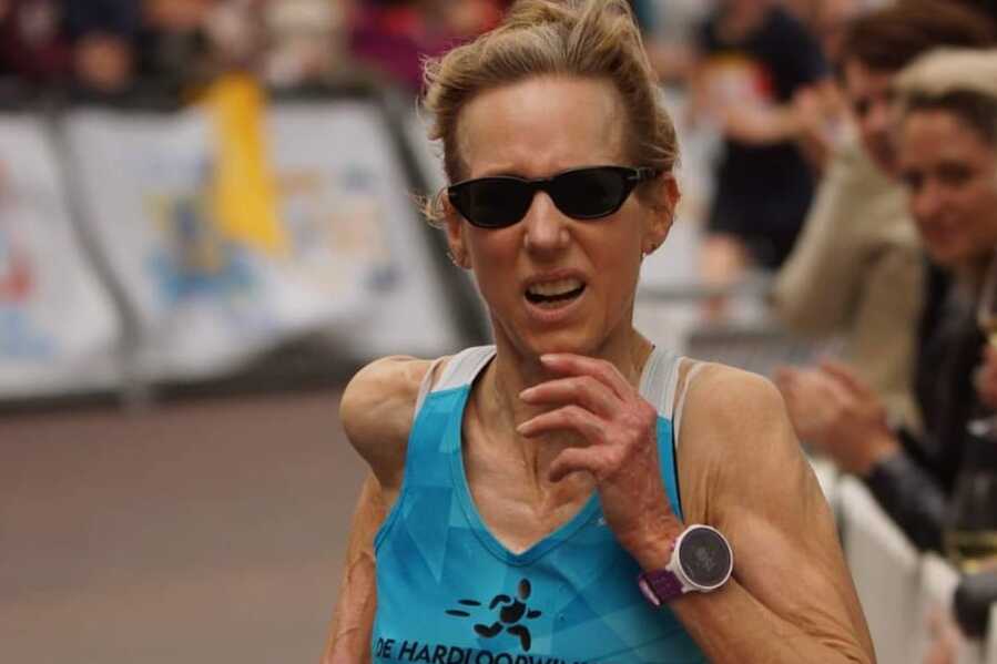 Läuferin im blauen Shirt mit Sonnenbrille, die beim Leiden Marathon den 10-km-Lauf absolviert. Zuschauer applaudieren im Hintergrund.
