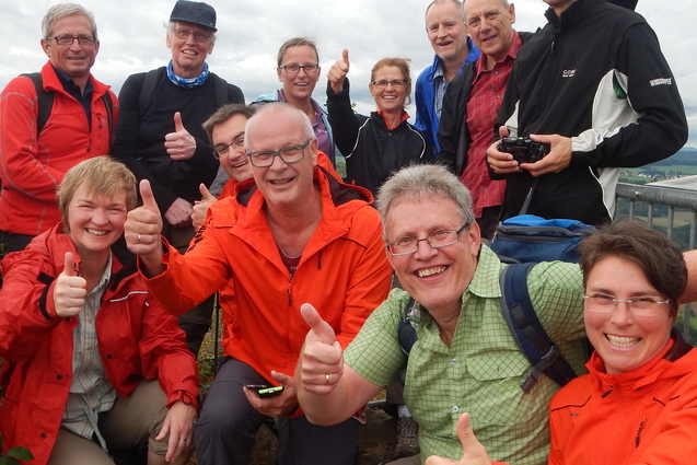 Gruppe von zehn Personen in Wanderkleidung, l&auml;chelnd und mit Daumen hoch, an einem Aussichtspunkt im Freien.