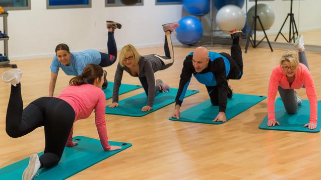 Fünf Personen machen Übungen auf Fitnessmatten in einem modernen Trainingsraum.