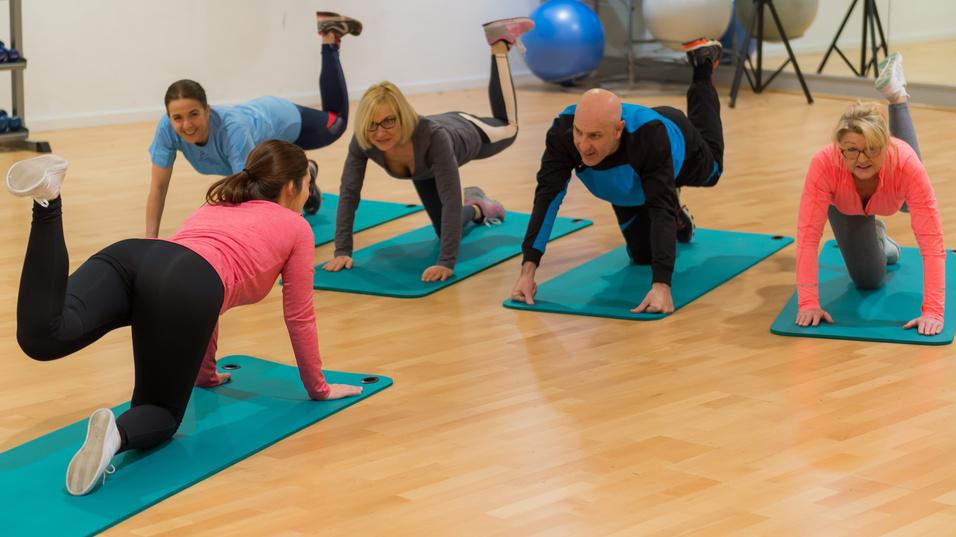 Fünf Personen machen Übungen auf Fitnessmatten in einem modernen Trainingsraum.