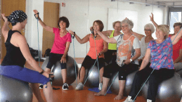 Gruppe von Frauen auf Gymnastikbällen, die an einer Fitnessstunde mit Übungsbändern teilnehmen.